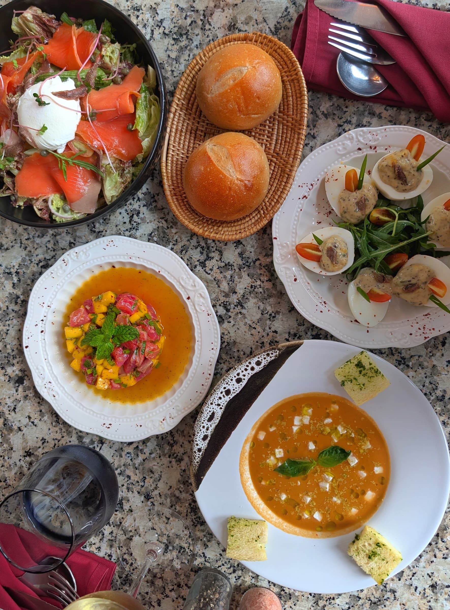 An overhead spread of shared starters at Somaha, including a salad, bread rolls, deviled eggs, and a tomato tartare
