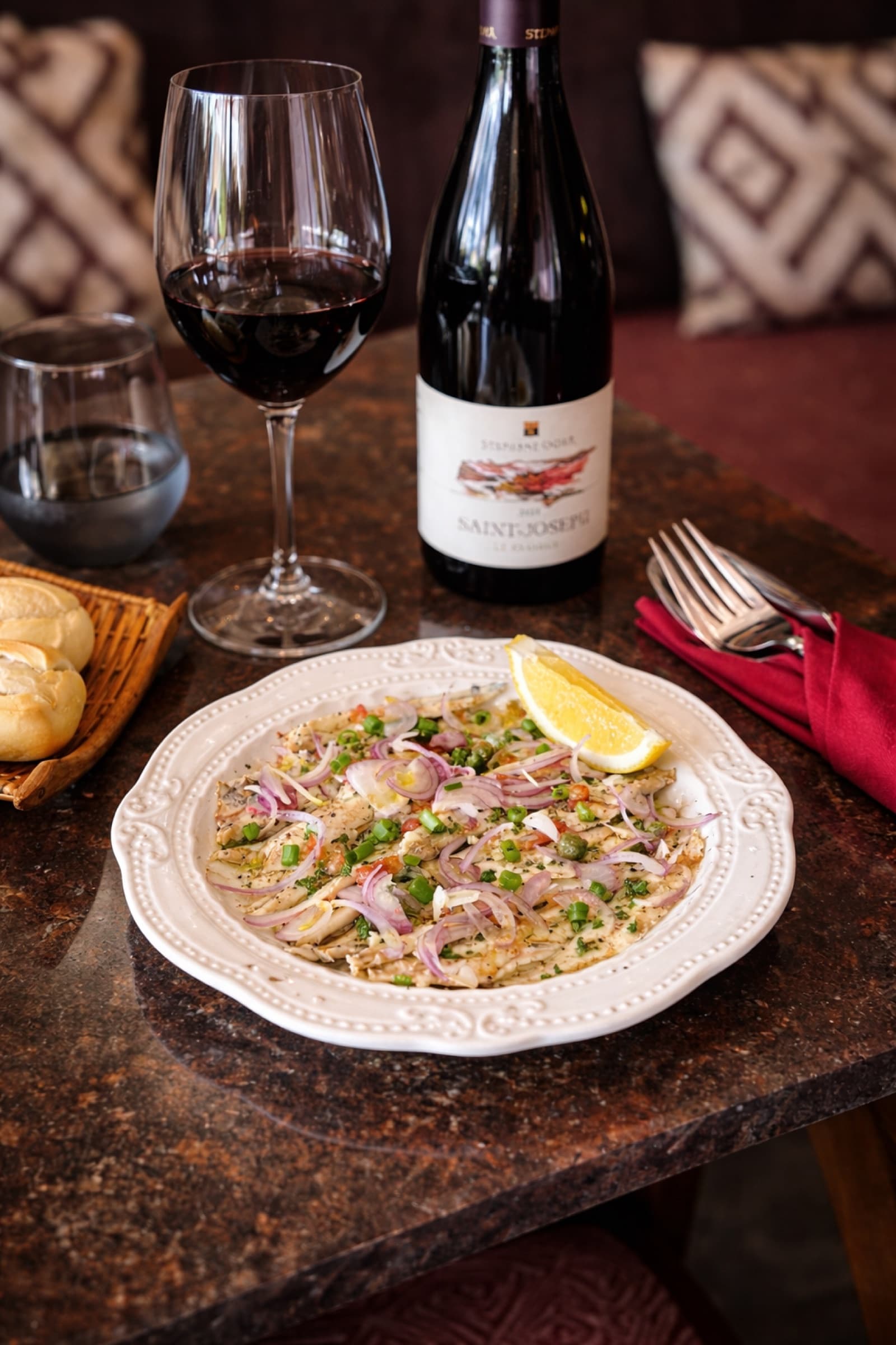 A citrus-cured fish crudo plate with a glass of Saint-Joseph red wine at Somaha