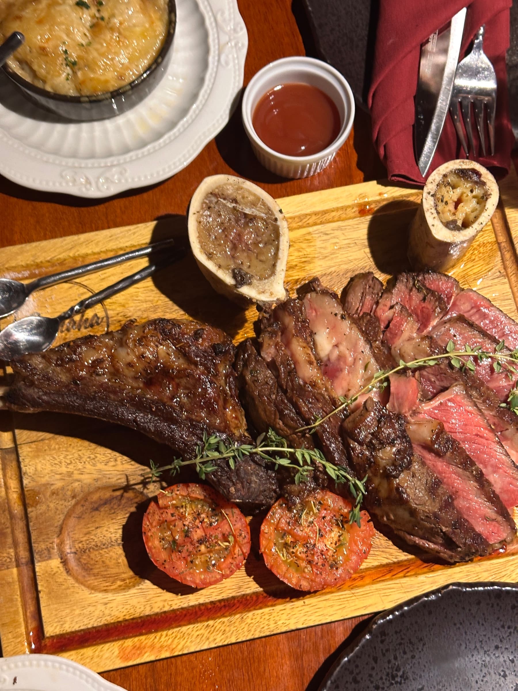 Top-down view of a sliced steak board with bone marrow and grilled tomatoes at Somaha